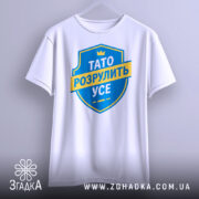 Футболка тато розрулить усе, підвішена на вішалці, з фронтального ракурсу, фон світлий, принт у вигляді синього щита з жовтою стрічкою та текстом.