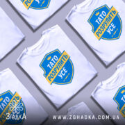 Футболка тато розрулить усе, розкладена на столі в хаотичному порядку, з верхнім ракурсом, фон світлий, принт у вигляді синього щита з жовтою стрічкою та текстом.