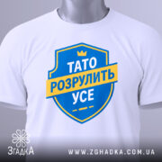 Футболка тато розрулить усе, білого кольору, зображена на манекені з легким боковим ракурсом, фон нейтральний, принт у вигляді синього щита з жовтою стрічкою та текстом.