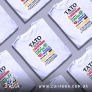 Футболка тато супергерой білого кольору, зображена на манекені, фон нейтральний, принт містить різнокольорові символи супергероїв та текст, що описує тата як супергероя.