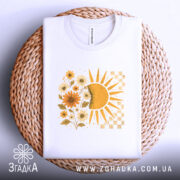 Футболка тепло життя. Біла футболка, складена на плетеній кошику, з принтом сонця і квітів жовтого кольору. Фон світло-сірий, футболка виглядає акуратно.