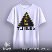 Футболка терпець білого кольору, підвішена на вішалці, ракурс спереду, фон світло-сірий, принт у вигляді жовтого трикутника з чорним написом 'ТЕРПЕЦЬ' та зображенням батареї з 1% заряду.