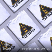 Футболка терпець білого кольору, зображена на манекені, ракурс спереду, фон світло-сірий, принт у вигляді жовтого трикутника з чорним написом 'ТЕРПЕЦЬ' та зображенням батареї з 1% заряду.