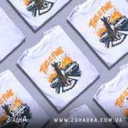 Футболка this is fine, біла, зображена на манекені, фон світло-сірий, принт з собакою на фоні двох автомобілів, яскраві кольори: оранжевий, чорний, жовтий.