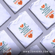 Футболка токсік бусінка, біла, зображена на манекені, фон градієнтний сірий, принт містить текст у зеленому та оранжевому кольорах, з серцем та рослинними елементами.