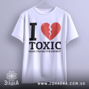 Футболка токсік енергія, білого кольору, підвішена на вішалці, фон світлий, принт з червоним розбитим серцем та чорним текстом 'I LOVE TOXIC MAIN CHARACTER ENERGY'.
