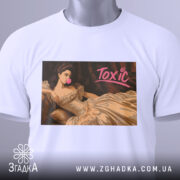 Футболка токсік білого кольору, складена на поверхні, з принтом, що зображує жінку в елегантній сукні, яка жує жувальну гумку. На футболці видно етикетку з зеленим шнурком. Принт має яскравий напис 'Toxic'.