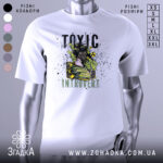 Футболка токсичний інтроверт, білого кольору, зображена на манекені з правого боку, фон світло-сірий, принт з дівчиною в протигазі та зеленим димом, текст 'TOXIC INTRUVERT' в чорному та зеленому кольорах.