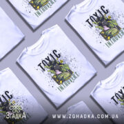 Футболка токсичний інтроверт, білого кольору, зображена на манекені з правого боку, фон світло-сірий, принт з дівчиною в протигазі та зеленим димом, текст 'TOXIC INTRUVERT' в чорному та зеленому кольорах.