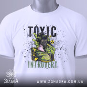 Футболка токсичний інтроверт, білого кольору, зображена на столі з верхнього ракурсу, фон світло-сірий, принт з дівчиною в протигазі, текст 'TOXIC INTRUVERT' в чорному та зеленому кольорах, на футболці є етикетка з зеленим шнурком.