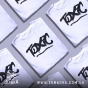 Футболка токсичний подарунок, біла, зображена на манекені, фон світло-сірий, принт чорний з написом 'TOXIC' у стилі графіті.