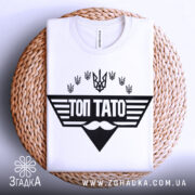 Футболка топ тато білого кольору, складена на плетеній основі, фон світлий, принт чорного кольору з написом 'ТОП ТАТО' та символікою України.