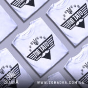 Футболка топ тато білого кольору, зображена з близького ракурсу на манекені, фон світлий, принт чорного кольору з написом 'ТОП ТАТО' та символікою України.