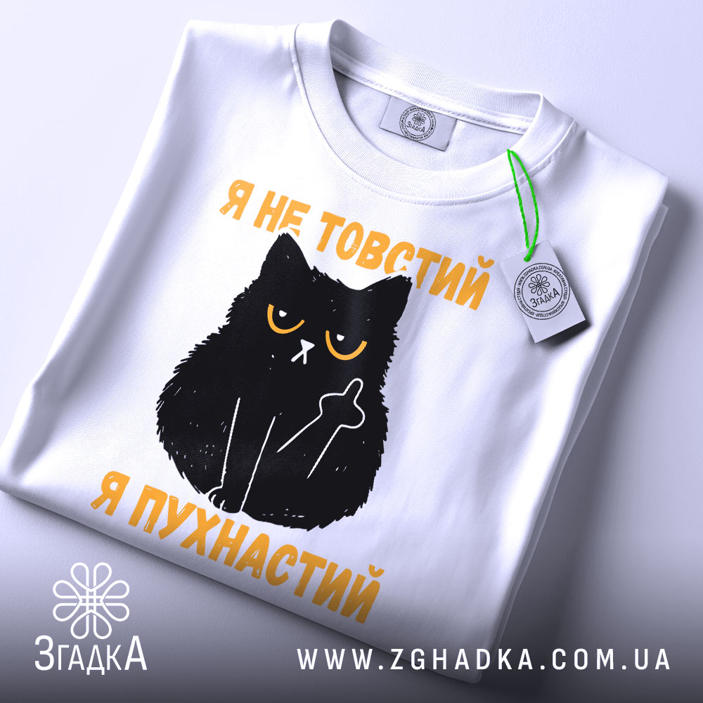 Футболка товстий пухнастий, біла, зображена зверху, на фоні світло-сірого кольору, принт з чорним котом з жовтими очима та текстом "Я не товстий, я пухнастий" у жовтому кольорі, з етикеткою на зеленій стрічці.