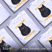 Футболка товстий пухнастий, біла, зображена з фронтального ракурсу, на фоні світло-сірого кольору, принт з чорним котом з жовтими очима та текстом "Я не товстий, я пухнастий" у жовтому кольорі.