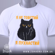 Футболка товстий пухнастий, біла, зображена зверху, на фоні світло-сірого кольору, принт з чорним котом з жовтими очима та текстом "Я не товстий, я пухнастий" у жовтому кольорі, з етикеткою на зеленій стрічці.