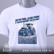 Футболка трактор у полі, біла, складена на столі, фон світлий, принт з трактором та текстом синього кольору, на футболці є етикетка.