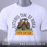 Футболка тракторист білого кольору, складена на столі, фон світло-сірий, принт з жовтим трактором та написом "Катаюсь там, де вовки, срати бояться!", на комірці видна етикетка.