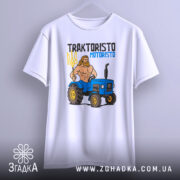 Футболка Трактористо мотористо білого кольору, підвішена на вішалці, з принтом, що зображає м'язистого чоловіка з тризубом і синім трактором. Фон однорідний, з легким градієнтом.