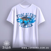 Футболка tralalero tralala, білого кольору, зображена з ракурсу спереду, підвішена на вішалці, фон світлий, принт з акулами та кросівками на блакитних хвилях.