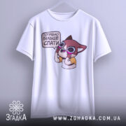 Футболка треба більше спати. Біла футболка, підвішена на вішалці, з принтом мультяшного персонажа, що має вираз обличчя, що говорить про потребу спати. Фон світло-сірий, що робить акцент на футболці.