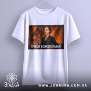 Футболка трохи божевільна, білого кольору, з прямим ракурсом, на фоні світло-сірого, з великим принтом, що зображує жінку в чорному костюмі на фоні палаючого будинку.