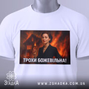 Футболка трохи божевільна, білого кольору, з верхнього ракурсу, на фоні світло-сірого, з великим принтом, що зображує жінку в чорному костюмі, а також з етикеткою на зеленому шнурку.