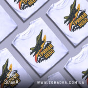 Футболка тримай небо. Біла футболка на манекені, з принтом літака, що летить через хмари, з написом 'ТРИМАЙ НЕБО' у чорному кольорі. Фон світло-сірий, деталі принта яскраві, з червоними та жовтими акцентами.