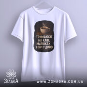 Футболка тримаюся на каві, білого кольору, підвішена на вішалці, фон світло-сірий, принт з чашкою кави та текстом на чорному фоні.