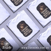 Футболка тримаюся на каві, кілька складених футболок білого кольору, фон світло-сірий, принт з чашкою кави та текстом на чорному фоні.