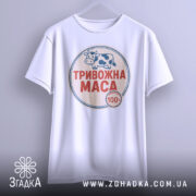 Футболка тривожна маса, біла, підвішена на вішалці, фон світло-сірий, принт з коровою та написом "ТРИВОЖНА МАСА" червоного кольору.