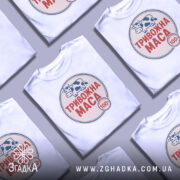 Футболка тривожна маса, біла, зображена на манекені з правого боку, фон світло-сірий, принт з коровою та написом "ТРИВОЖНА МАСА" червоного кольору.