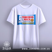 Футболка тривожна маса білого кольору, підвішена на вішалці, фон світлий, принт з коровою та текстом "ТРИВОЖНА МАСА" чітко видимий.