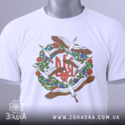 Футболка Тризуб Лелеки, біла, складена на поверхні, фон світло-сірий, принт з тризубом та лелеками, на футболці є етикетка з зеленим шнурком.