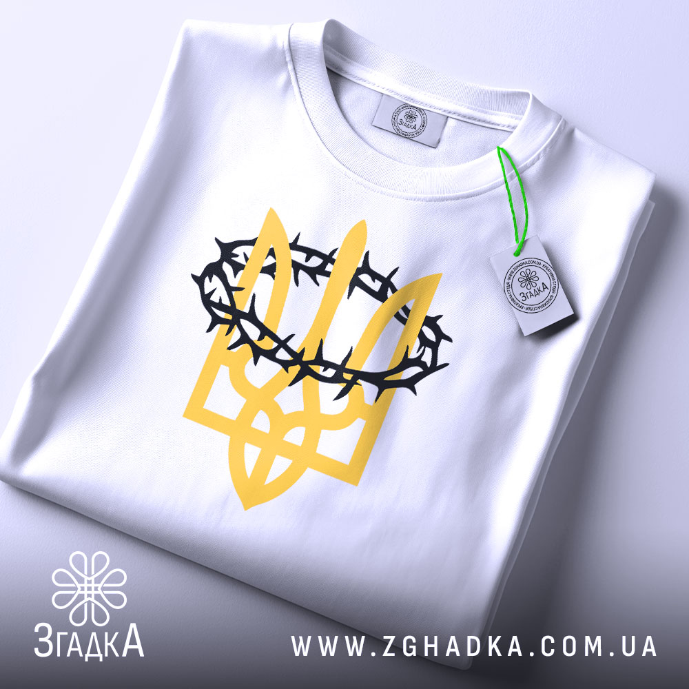 Футболка тризуб терни білого кольору, складена на поверхні, фон світло-сірий, принт у вигляді тризуба жовтого кольору з чорними тернами, на комірці видно етикетку.