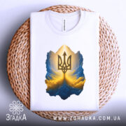 Футболка тризуб золото, біла, зображена зверху на плетеному кошику, фон світлий, принт з тризубом у золотих та блакитних тонах, з чітким контуром.