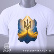 Футболка тризуб золото, біла, зображена зверху, на столі, фон світлий, принт з тризубом у золотих та блакитних тонах, з етикеткою зеленого кольору.