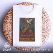 Футболка це братерство, складена біла футболка на плетеній кошику, з принтом, на якому зображені дві з'єднані руки, що тримають меч, а над ними літає голуб, фон принта темно-синій з червоними квітами, деталі принта включають блискавки.