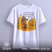 Футболка це добре, біла, підвішена на вішалці, з принтом собаки в капелюсі, що сидить на стільці біля столу з чашкою, оточений полум'ям. Принт яскравий, фон нейтральний.