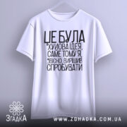 Футболка це погана ідея. Біла футболка, підвішена на вішалці, з чорним принтом. Фон світло-сірий, текст чіткий і контрастний, розташований по центру.