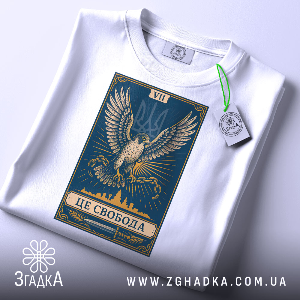 Футболка це свобода, біла футболка, складена на поверхні, принт з орлом на синьому фоні, ракурс зверху, фон світлий, на футболці є етикетка з зеленим шнурком.