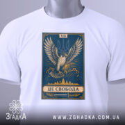 Футболка це свобода, біла футболка, складена на поверхні, принт з орлом на синьому фоні, ракурс зверху, фон світлий, на футболці є етикетка з зеленим шнурком.