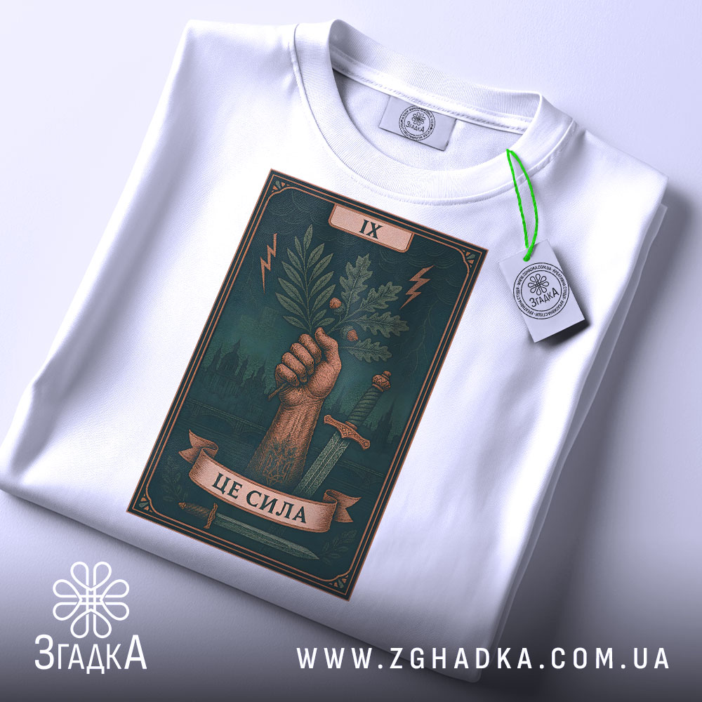 Футболка це сила. Біла футболка, складена на поверхні, з видимим принтом, зображена з верхнього ракурсу. Принт з рукою, що тримає гілку, на фоні темно-зеленого кольору, з елементами блискавок і мечів, з етикеткою, що звисає.