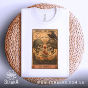 Футболка це війна. Біла футболка, складена на плетеній кошику, з принтом черепів у військових шоломах, червоними маківками та чорним вороном. Вид зверху, фон світлий, текстура кошика додає контрасту.