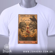 Футболка це війна. Біла футболка, складена на поверхні, з принтом черепів у шоломах, червоними квітами та чорним вороном. Вид з верхнього ракурсу, на футболці є етикетка з зеленим шнурком, фон світлий.