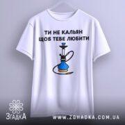 Футболка ти не кальян. Біла футболка з коротким рукавом, підвішена на вішалці, зображена з фронтального ракурсу. Принт на грудях з текстом 'ТИ НЕ КАЛЬЯН ЩОБ ТЕБЕ ЛЮБИТИ' та малюнком кальяну. Фон світлий, з легким градієнтом.