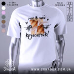 Футболка ти ж мій круасанчик. Біла футболка з коротким рукавом, зображена з правого ракурсу. На фоні світло-сірий колір. Принт з двома круасанами, обв'язаними стрічкою, та написом "ти ж мій круасанчик!" у чорному кольорі.