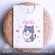 Футболка ти ж моя жопка, біла, складена на плетеній основі, фон світлий, принт з двома котиками, один з яких обіймає іншого, навколо рожеві сердечка.