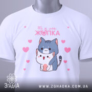 Футболка ти ж моя жопка, біла, складена на поверхні, фон світлий, принт з двома котиками, один з яких тримає іншого, навколо рожеві сердечка, на комірці є етикетка.