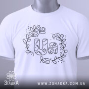 Футболка UA квіти, біла, складена на столі, з верхнього ракурсу, фон світло-сірий, принт з написом UA в оточенні квітів і листя, виконаний чорним кольором, з етикеткою зеленого кольору.